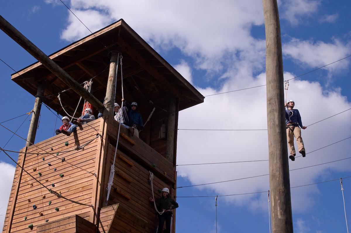 Students sit in a high ropes course tower, atop a rock wall at newbb电子平台